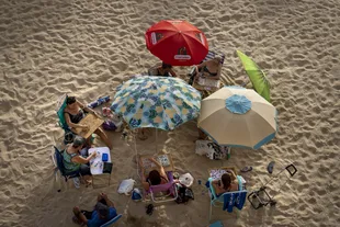Group of women playing bingo while protecting themselves from the sun and sitting under umbrellas on the beach of Cadiz